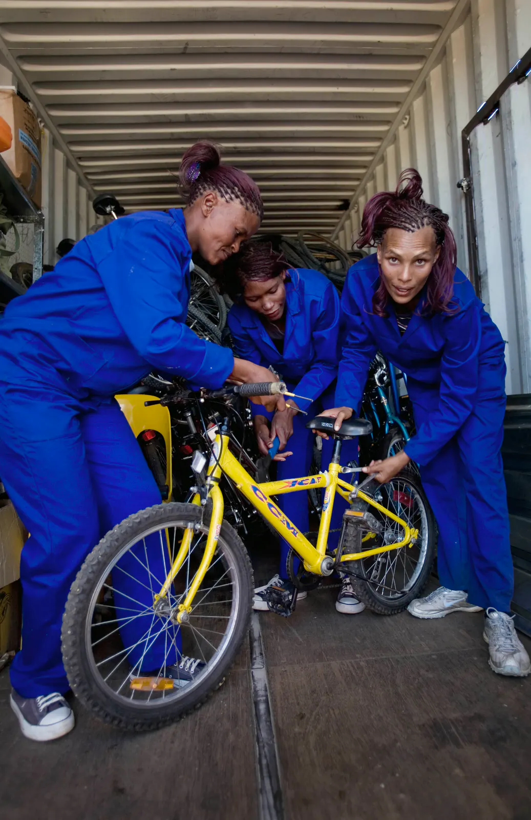 Tres personas con monos de trabajo ajustando una bicicleta en el taller