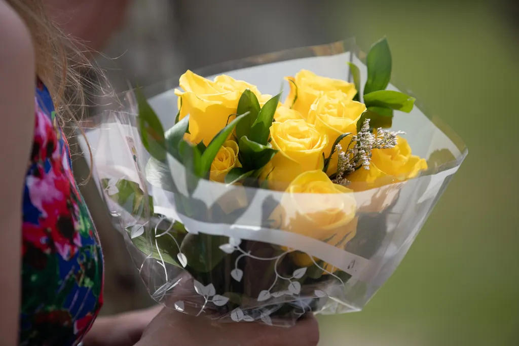 Mains tenant un bouquet de roses jaunes emballé dans du papier